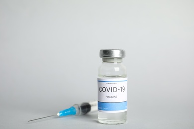 Vial with coronavirus vaccine and syringe on light background