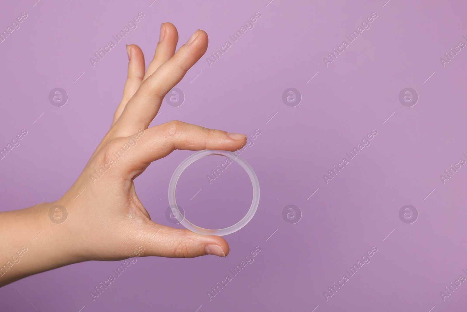 Photo of Woman holding diaphragm vaginal contraceptive ring on lilac background, closeup. Space for text