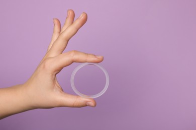 Photo of Woman holding diaphragm vaginal contraceptive ring on lilac background, closeup. Space for text