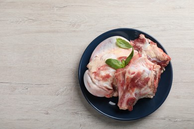 Photo of Plate with raw chopped meaty bones and basil on white wooden table, top view. Space for text