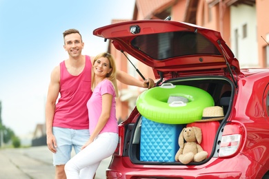 Photo of Happy couple near car trunk with suitcases outdoors