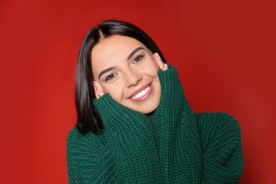 Happy young woman wearing warm sweater on red background