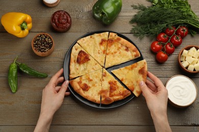 Photo of Top view of woman taking delicious khachapuri piece with cheese at wooden table