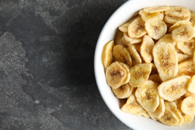 Photo of Bowl with sweet banana slices on grey background, top view with space for text. Dried fruit as healthy snack