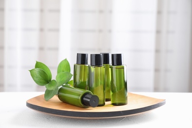 Wooden plate with mini bottles of cosmetic products on white table indoors