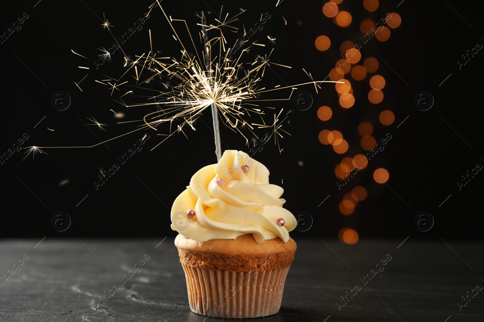 Image of Birthday cupcake with sparkler on table against dark background