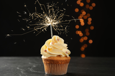 Birthday cupcake with sparkler on table against dark background