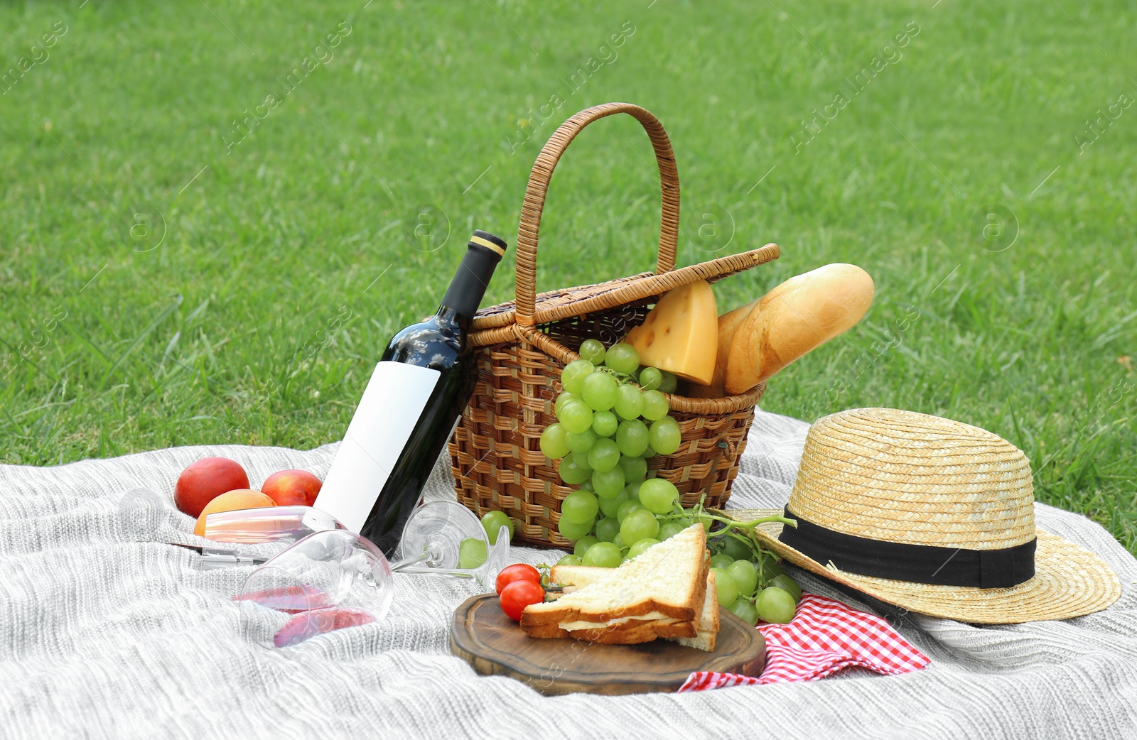 Photo of Basket with food and straw hat on blanket in park. Summer picnic