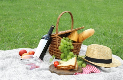 Basket with food and straw hat on blanket in park. Summer picnic