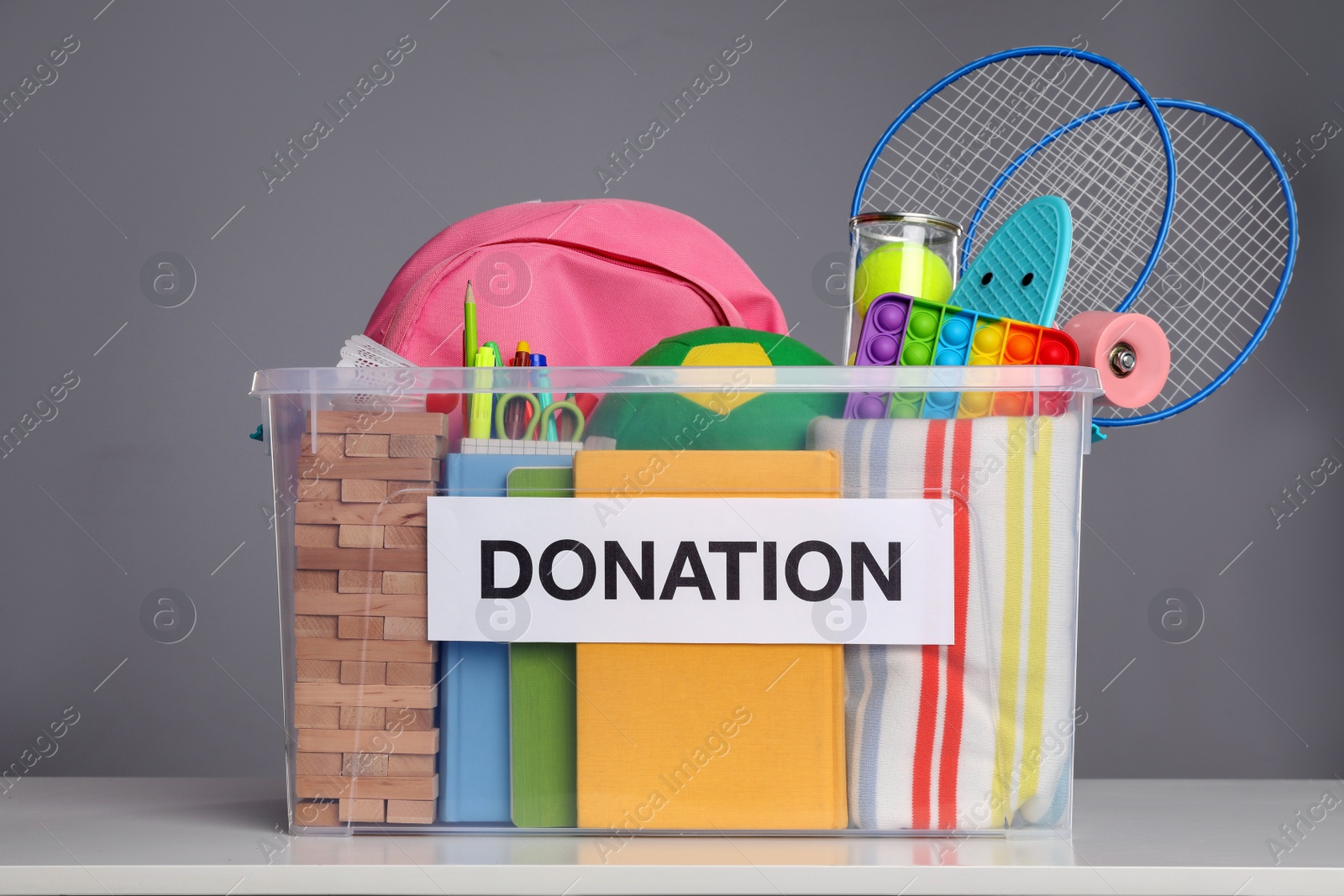 Photo of Donation box with different toys and stationery on white table against grey background