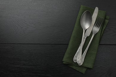 Photo of Stylish setting with cutlery and napkin on black wooden table, top view. Space for text