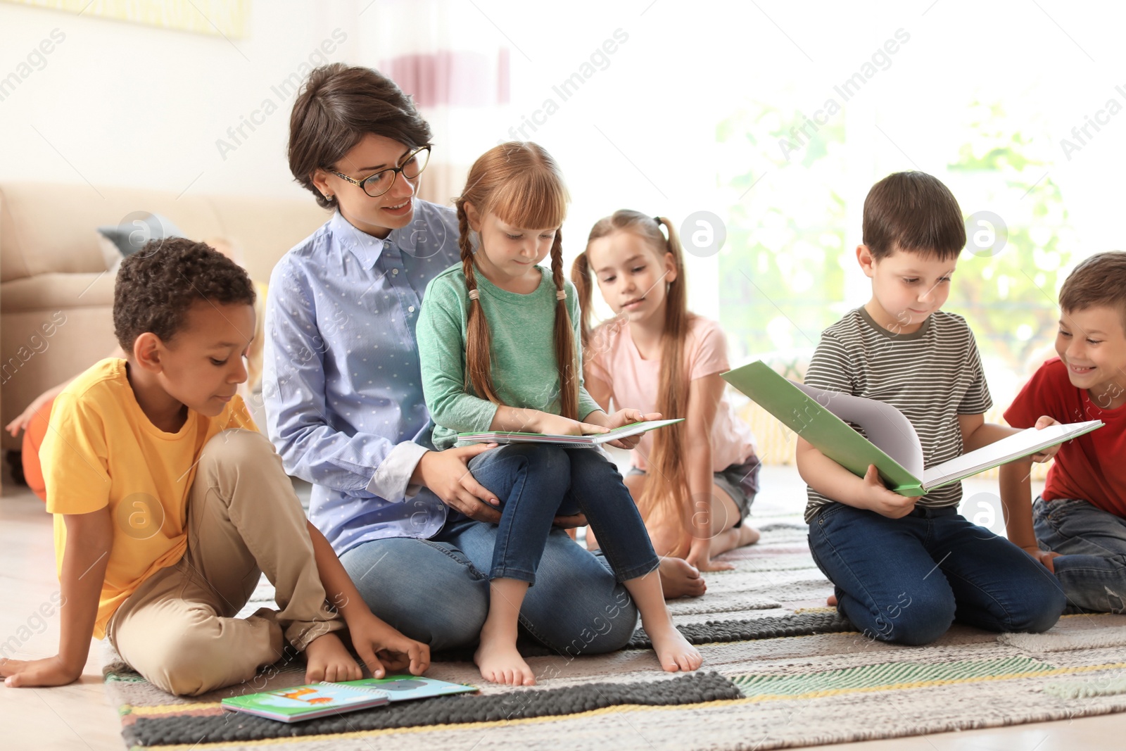 Photo of Young woman reading book to little children indoors. Learning by playing