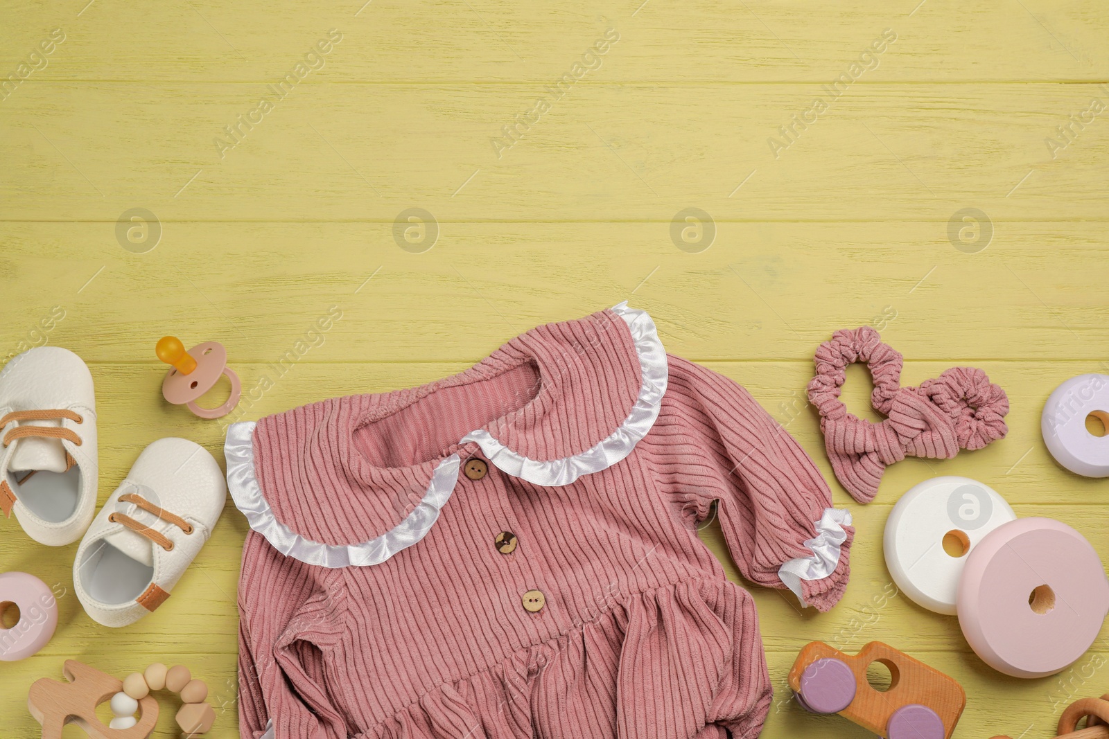 Photo of Flat lay composition with baby clothes and accessories on yellow wooden table. Space for text