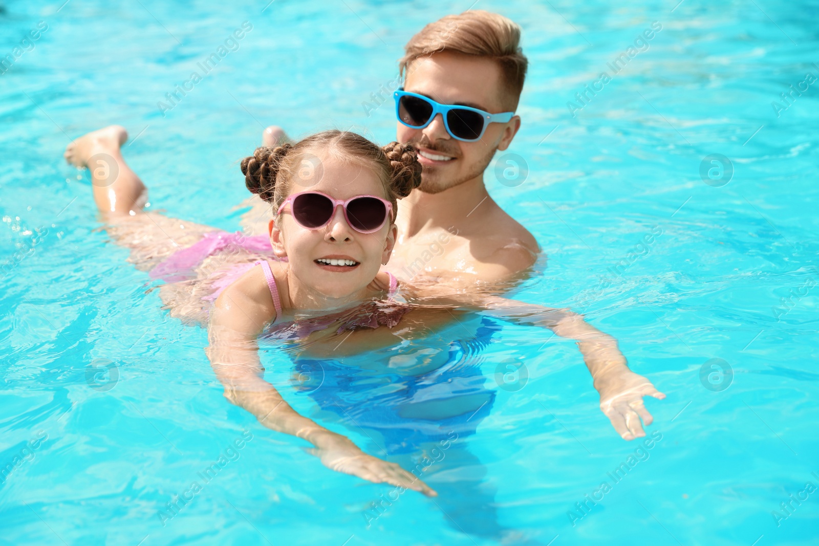 Photo of Young man teaching his daughter to swim in pool