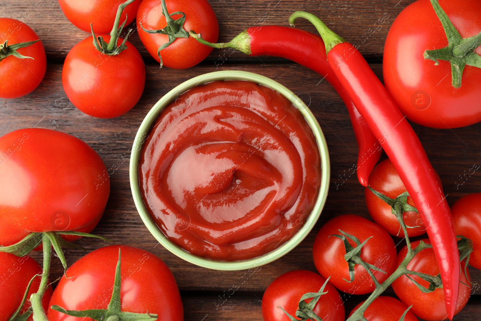 Photo of Bowl of tasty ketchup, chili peppers and tomatoes on wooden table, flat lay