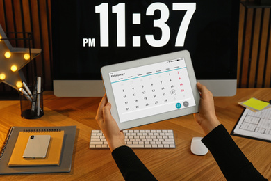 Photo of Woman using tablet with calendar app at workplace, closeup
