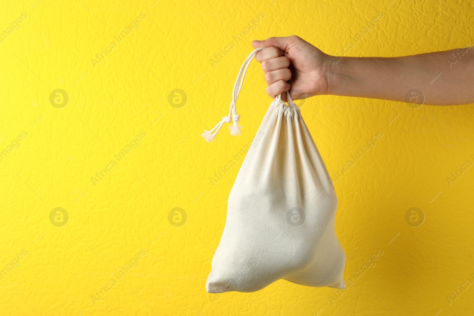 Photo of Woman holding full cotton eco bag on yellow background, closeup. Space for text