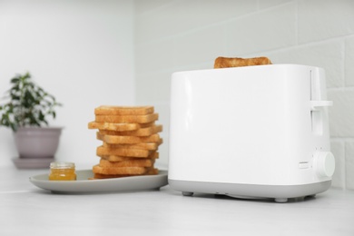 Photo of Modern toaster with slices of bread and honey on white table in kitchen