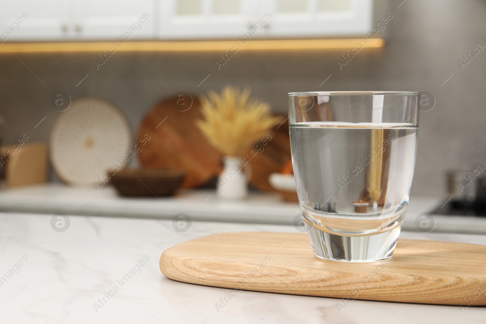 Photo of Filtered water in glass on white marble table in kitchen, closeup. Space for text