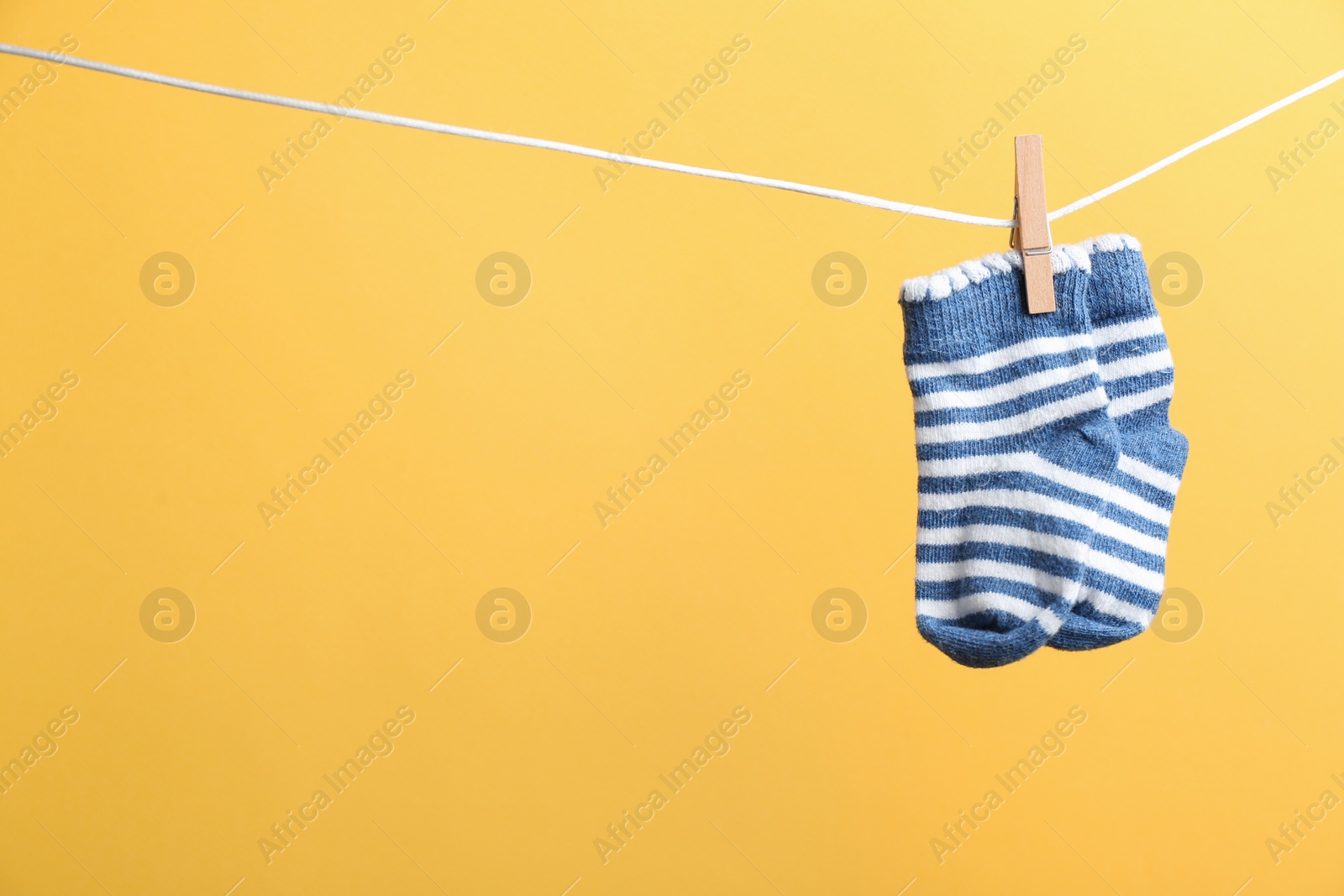 Photo of Small socks hanging on washing line against color background, space for text. Baby accessories