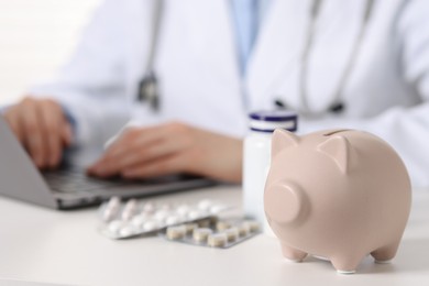 Photo of Doctor using laptop at white table, focus piggy bank