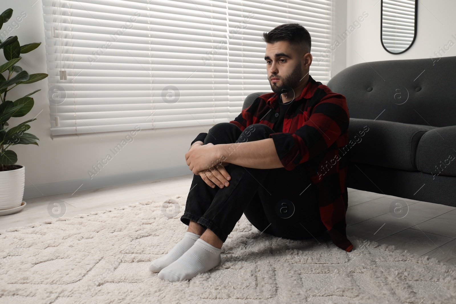 Photo of Sad man sitting on floor at home. Space for text