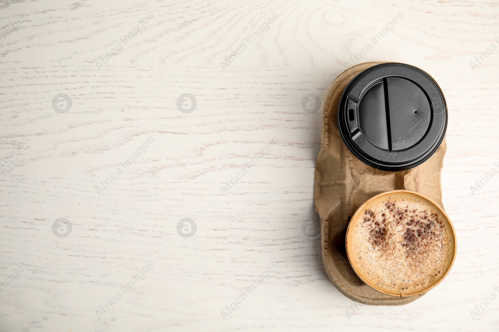 Photo of Takeaway paper cups with coffee in cardboard holder on white wooden table, top view. Space for text