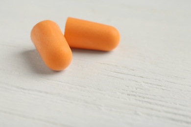 Photo of Pair of orange ear plugs on white wooden background, closeup. Space for text