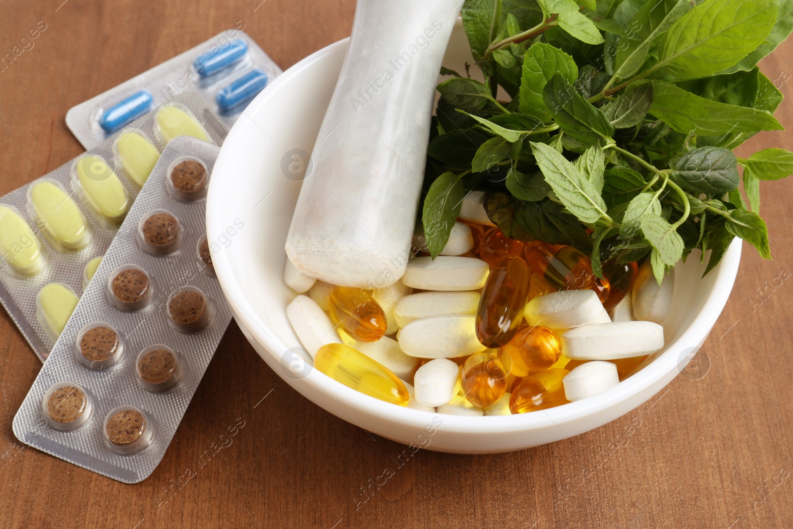 Photo of Mortar with fresh mint and pills on wooden table, closeup