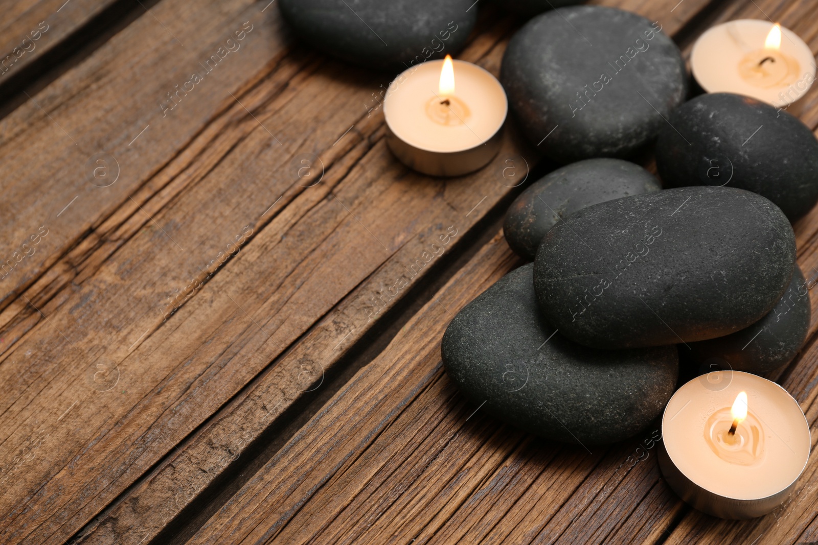 Photo of Spa stones and lit candles on wooden background, space for text
