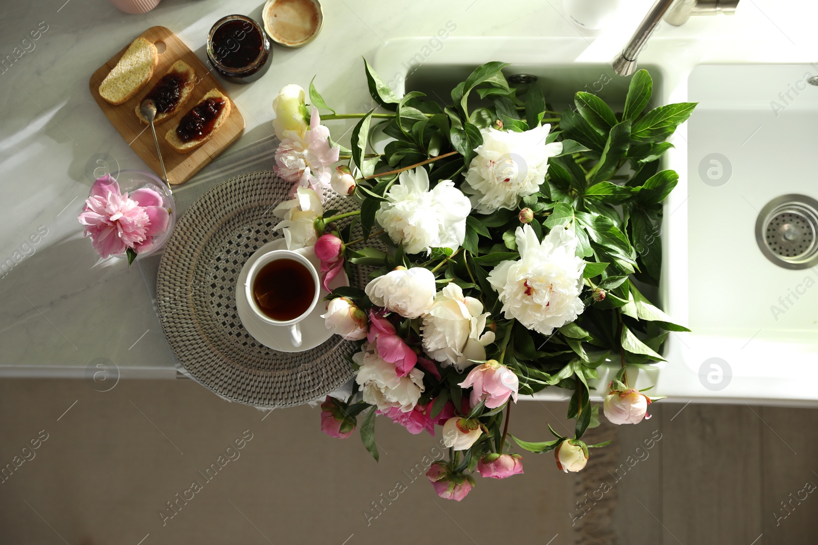 Photo of Beautiful peonies and breakfast on kitchen counter, flat lay