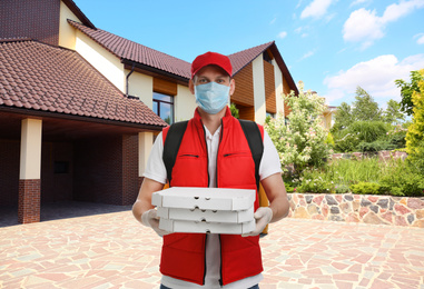 Courier in protective mask and gloves with order near house. Delivery service during coronavirus quarantine