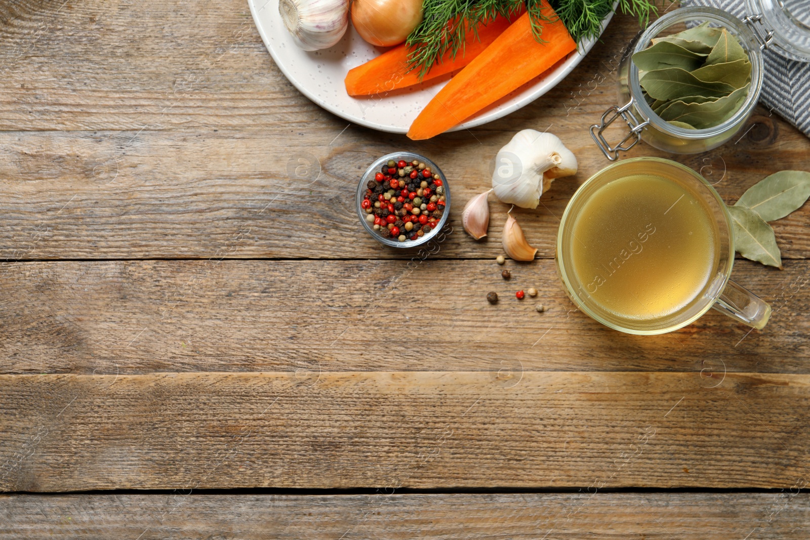 Photo of Hot delicious bouillon in glass cup and ingredients on wooden table, flat lay. Space for text