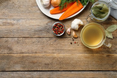 Hot delicious bouillon in glass cup and ingredients on wooden table, flat lay. Space for text