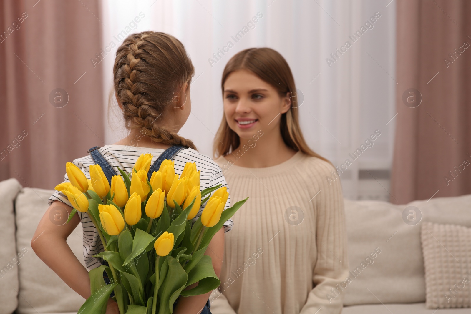 Photo of Little daughter congratulating mom with bouquet of yellow tulips at home. Happy Mother's Day