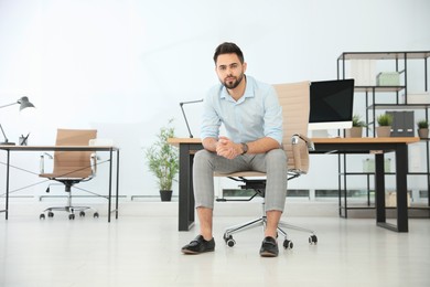 Young businessman sitting in office chair at workplace. Space for text