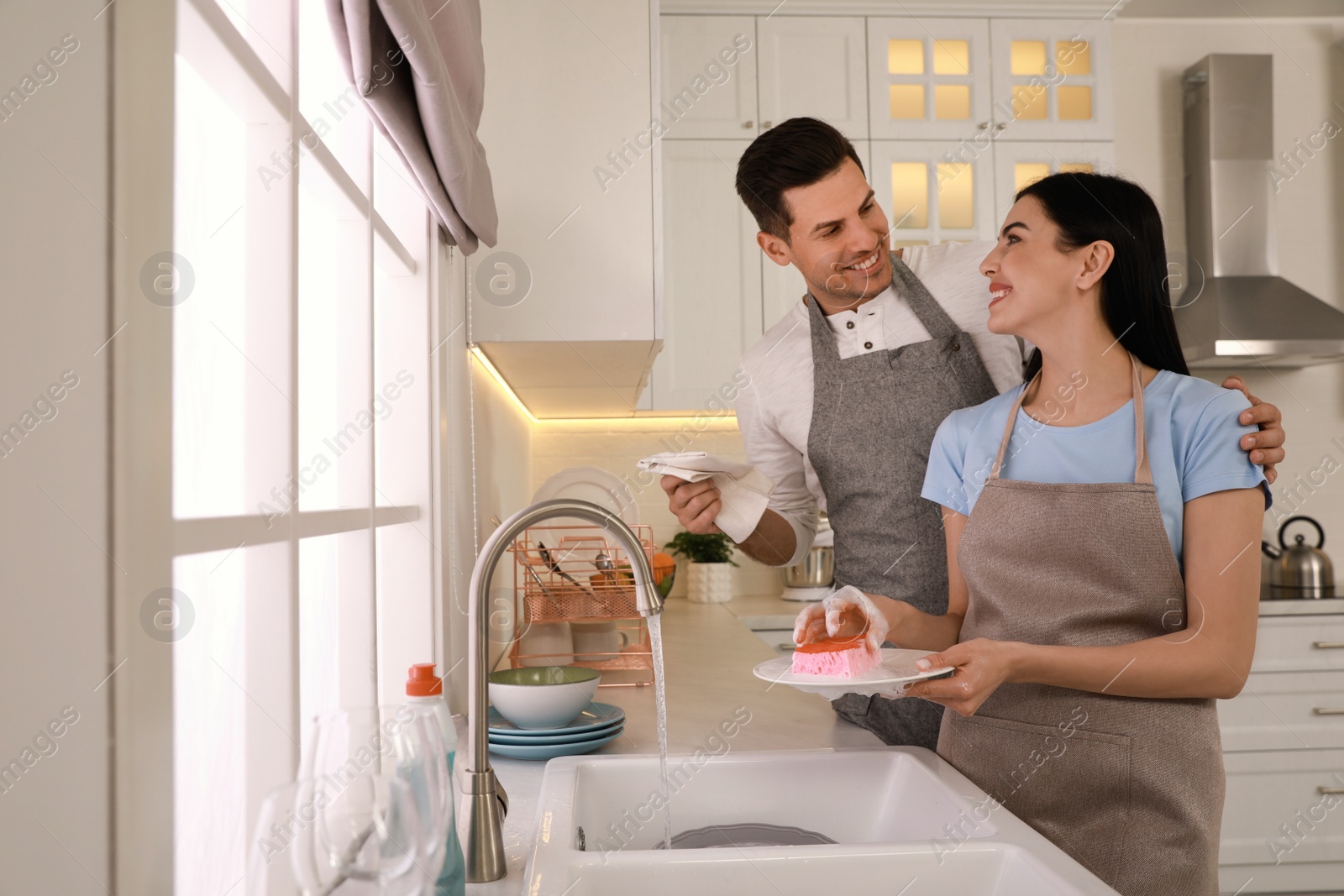 Photo of Happy lovely couple washing dishes in kitchen