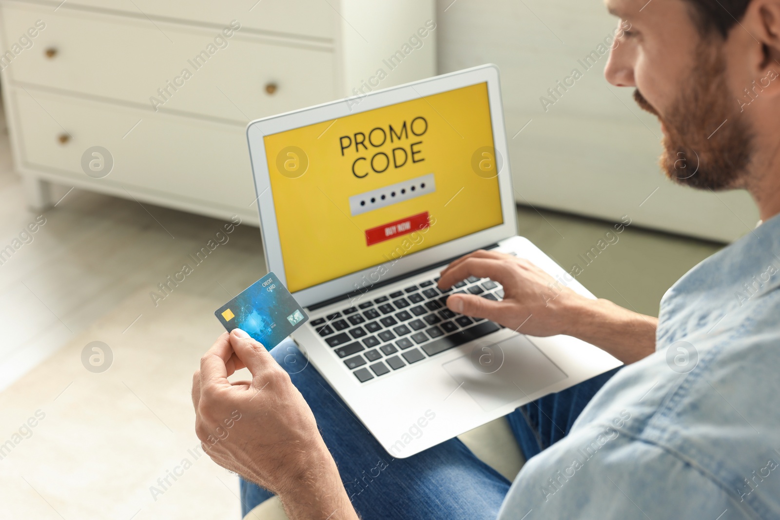 Photo of Man holding laptop with activated promo code and credit card indoors, closeup