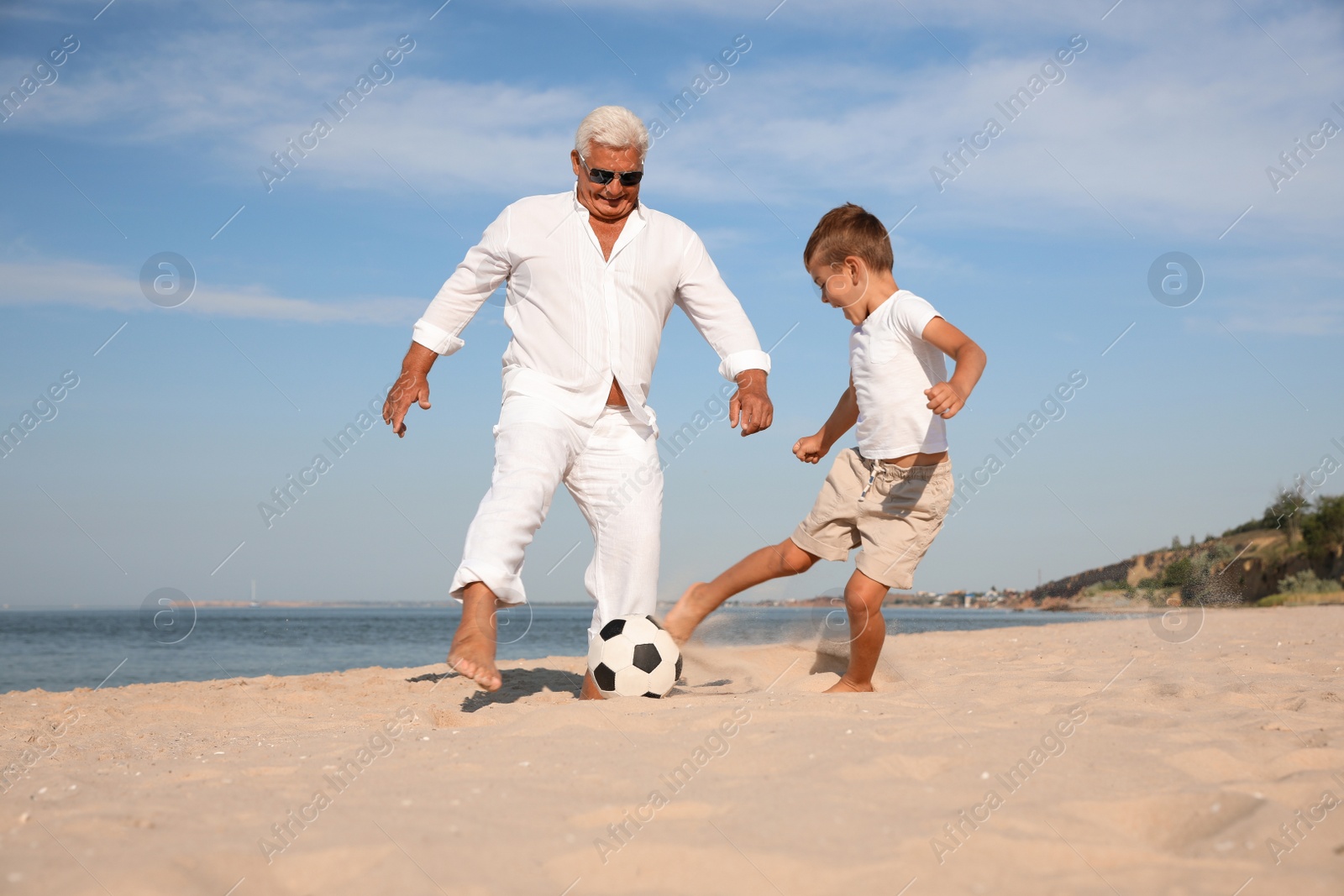 Photo of Cute little boy and grandfather playing with soccer ball on sea beach