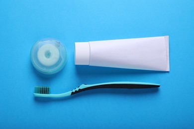 Container with dental floss, toothpaste and toothbrush on light blue background, flat lay