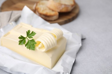 Photo of Tasty butter with curl and parsley on light grey table, closeup. Space for text