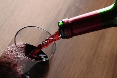 Pouring tasty red wine in glass at wooden table, closeup