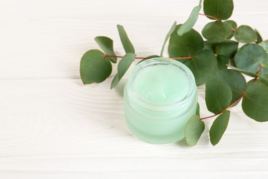 Photo of Homemade cosmetic product and eucalyptus leaves on white wooden table, closeup. Space for text