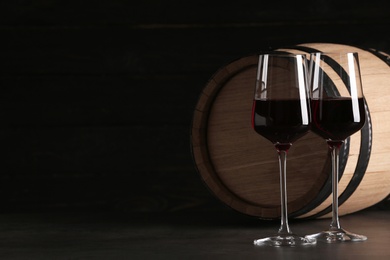 Photo of Glasses of red wine and wooden barrel on table against dark background. Space for text