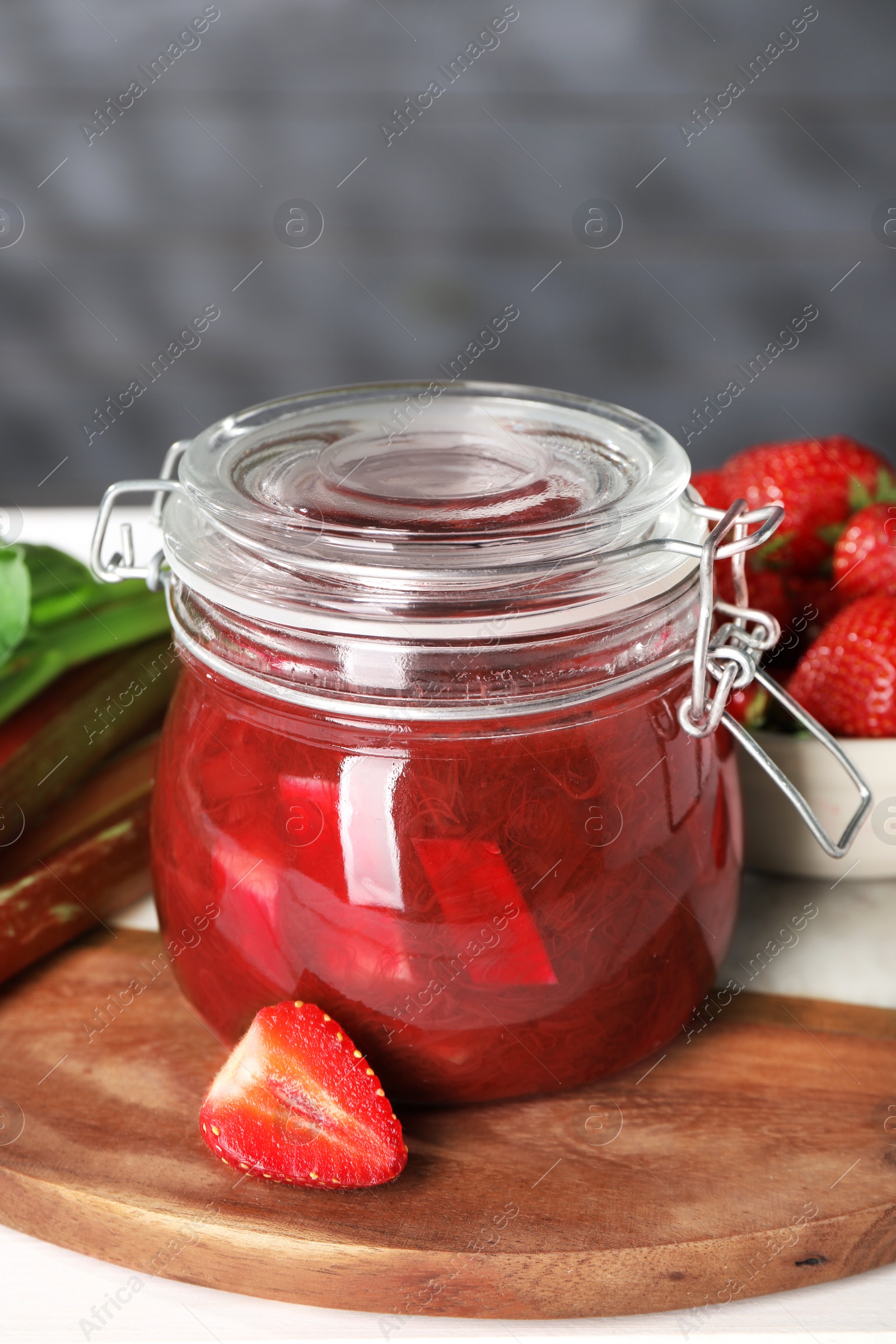 Photo of Jar of tasty rhubarb jam, and strawberry on white table, closeup