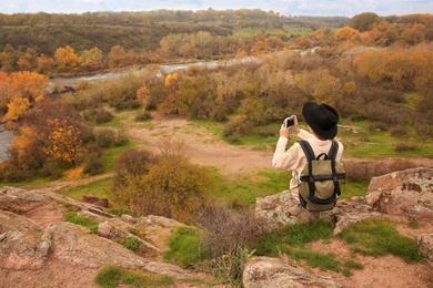 Woman with travel backpack taking photos in mountains, back view