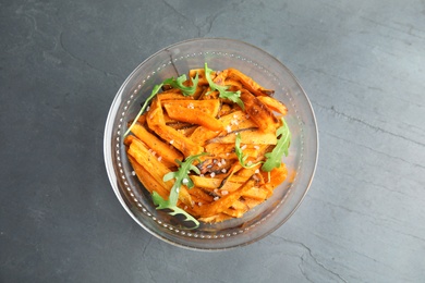 Photo of Glass bowl with baked sweet potato slices and arugula on grey background, top view