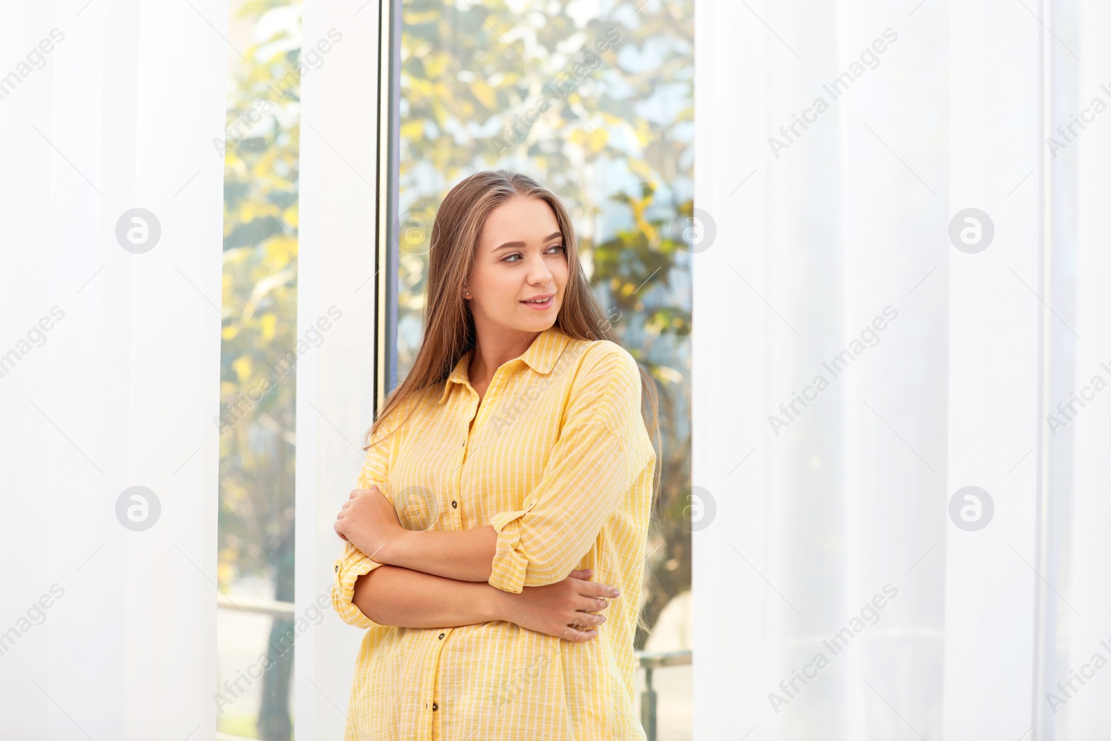 Photo of Young woman near window with open curtains at home