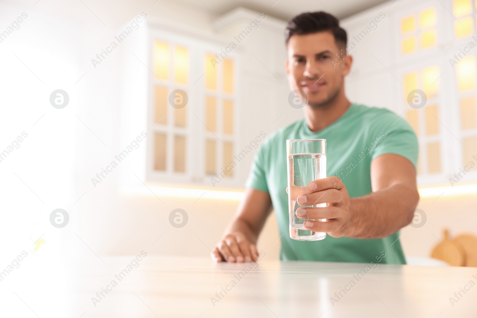 Photo of Man holding glass of pure water at table in kitchen, focus on hand. Space for text