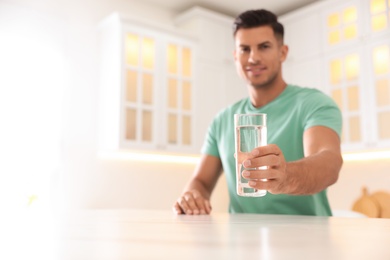 Man holding glass of pure water at table in kitchen, focus on hand. Space for text